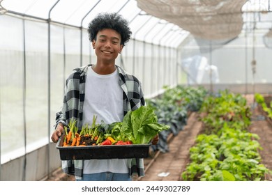 Happy African teenage boy holding a crate of organic vegetables in greenhouse garden. School student enjoy outdoor lifestyle learning and working with nature healthy food for sustainable living. - Powered by Shutterstock