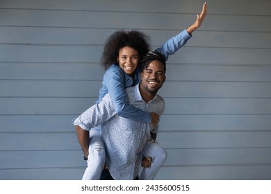 Happy African wife piggyback beloved husband with dreadlocks, wear casual clothes pose on blue wooden wall background. Beautiful 30s couple in love, romantic relationships, travel, vacation concept - Powered by Shutterstock