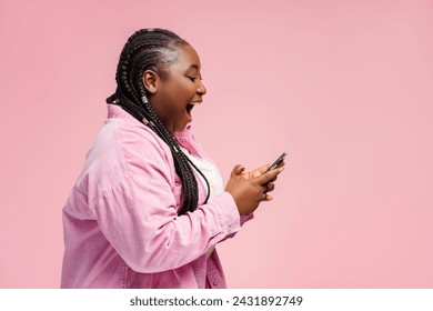 Happy African woman holding smartphone using mobile app, shopping online with sale, cash back isolated on pink background, copy space. Overjoyed female sports betting, win money, reading good news - Powered by Shutterstock