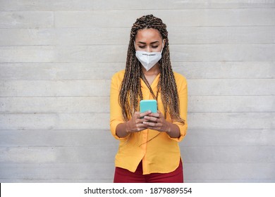 Happy african woman with protective face mask using mobile phone outdoors - Focus on face - Powered by Shutterstock