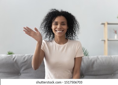 Happy african woman sit on couch wave hand looks at camera make video call use computer webcam view, instant virtual chat online communication, vlogger record webinar, job interview distantly concept