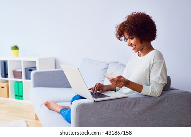 Happy african woman sitting on the sofa with laptop calculating home finances