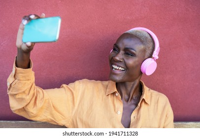 Happy African woman taking selfie with mobile smartphone while listening music with wireless headphones