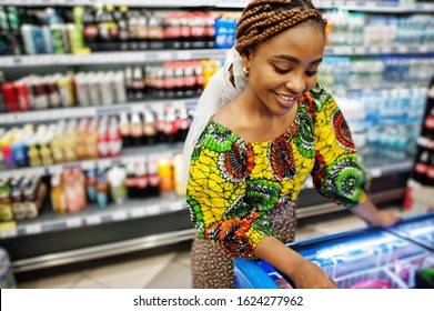 Happy African Woman In Traditional Clothes And Veil Looking Product At Grocery Store, Shopping In Supermarket.  Afro Black  Women Costumer Buying Food At The Market.