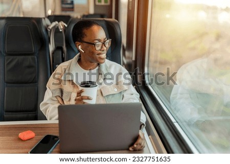 Happy African young businesswoman enjoying in train ride while drinking takeaway coffee. Business trips, tourist solo travel.