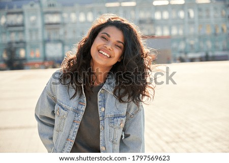 Happy African young woman wearing denim jacket laughing looking at camera standing on street. Smiling Afro American teen generation z hipster girl posing outdoor backlit with sunlight, portrait.