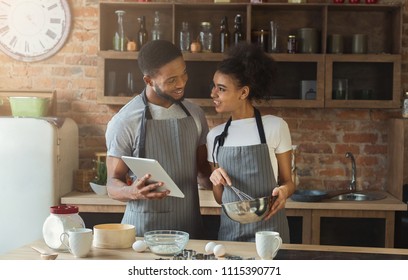 Happy African-american Couple Baking Pie And Using Digital Tablet In Loft Interior.