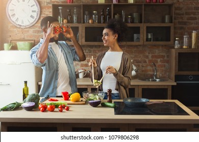 Happy african-american couple cooking healthy food and having fun together in their loft kitchen at home. Woman and man drinking wine. Preparing vegetable salad. - Powered by Shutterstock