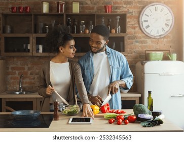 Happy african-american couple cooking healthy food and having fun together in their loft kitchen at home. Woman and man drinking wine. Preparing vegetable salad. - Powered by Shutterstock