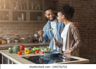 Happy african-american couple tasting dinner in loft kitchen at home