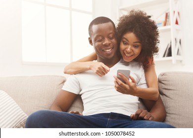 Happy African-american Couple Using Smartphone, Online Shopping Or Networking On Sofa At New Apartment, Copy Space