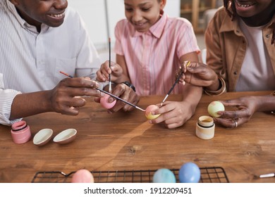 Happy African-American Family Painting Easter Eggs Together While Sitting At Wooden Table And Bonding Over DIY Project, Copy Space