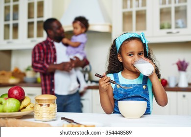 Happy African-American girl looking at camera while drinking milk