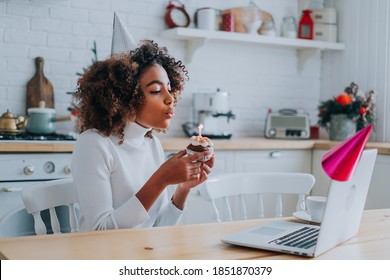 Happy African-American lady with modern haircut conducting online birthday party and blowing candle on cupcake closeup - Powered by Shutterstock