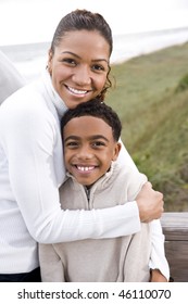 Happy African-American Mother And Ten Year Old Son Standing Together At Beach Hugging