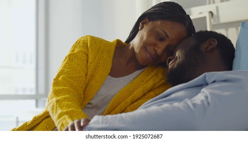 Happy African-american Wife Visiting Smiling Husband In Hospital. Portrait Of Sick Black Man Resting In Hospital Bed And Embracing Young Woman Visitor