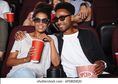 Happy Afro American Couple Watching 3D Movie And Eating Popcorn While Sitting In A Movie Theater