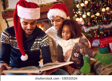 Happy Afro American Family Read A Book At Fireplace On Christmas Eve. Family With Child Celebrating Xmas
