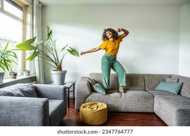 Happy afro american woman dancing on the sofa at home - Smiling girl enjoying day off lying on the couch - Healthy life style, good vibes people and new home concept - Powered by Shutterstock