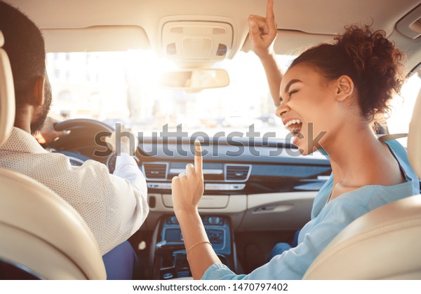 Happy afro couple driving in car and girl singing\
song, enjoy tavel by auto