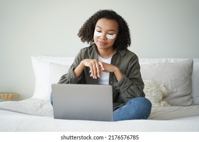 Happy Afro Girl Applies Eye Patches And Relaxing At Home In Weekend Morning. Young Hispanic Woman Having Rest Watching Tv Series. Skin Moisturizing. Lovely Curly Girl Is Grooming Herself In Bedroom.