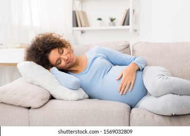 Happy afro pregnant woman napping on sofa, having sweet day dream and smiling, free space
