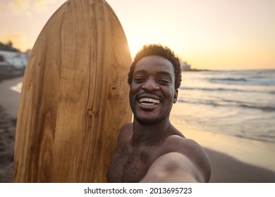 Happy Afro Surfer Having Fun Taking Selfie During Sunset Time - African Man Enjoying Surf Day - Extreme Sport Lifestyle People Concept 