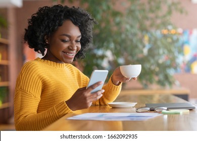 Happy afro woman drinking coffee and using mobile phone at cafe, copy space - Powered by Shutterstock