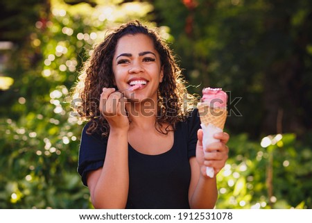 Happy afro woman eating ice cream in the park.