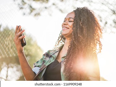 Happy afro woman having video call with smart cell phone in city park outdoor - African girl having fun using smartphone - New technology trends and millennials generation concept - Focus on face