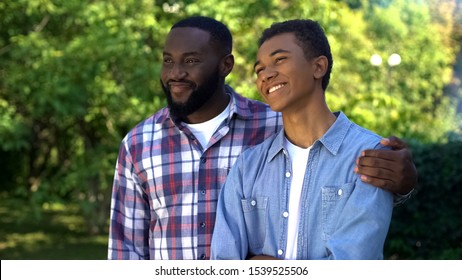 Happy Afro-american Dad Hugging Teenage Son Standing Outdoors Together, Love