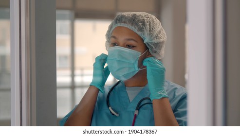 Happy Afro-american Woman Surgeon Removing Mask And Smiling After Successful Surgery. Portrait Of Cheerful Black Female Nurse In Protective Uniform Putting Off Mask And Relaxing