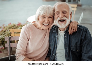 Happy aged couple. Positive aged woman sitting with her husband while hugging him