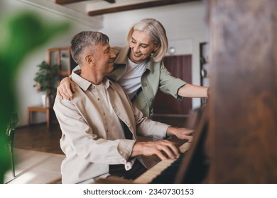 Happy aged female in casual clothes hugging man playing melody on piano during weekend together at home looking at each other and smiling - Powered by Shutterstock