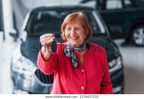 Happy aged woman in formal wear stands in front of\
modern white car.