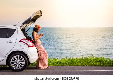 Happy alone young woman traveler on the beach road with white hatchback car with hand holding mobile phone and sea beach background. Traveler car in summer concept - Powered by Shutterstock