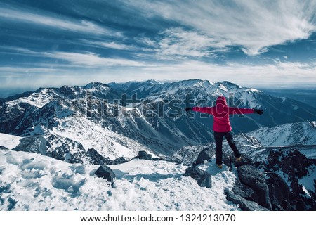 Happy alpinist girl standing at snow covered top of the peak of Jebel Toubkal in Atlas mountains Morocco