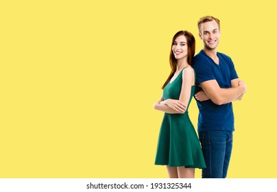 Happy amazed amorous couple. Portrait of young models standing back to back pose, in love concept, isolated over yellow color background. Smiling man and woman at studio. Copy space.