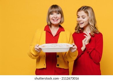 Happy Amazed Cool Woman 50s In Red Shirt Have Fun With Teenager Girl 12-13 Years Old. Grandmother Granddaughter Hold Meal Dish Casserole Isolated On Plain Yellow Background. Family Lifestyle Concept