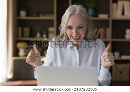 Happy amazed senior laptop user woman getting exciting good news from online chat, email letter, notice, video call, looking at screen, staring at monitor, laughing, smiling, making winner hands