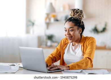 Happy amazed successful young african american woman, manager, freelancer or student working or studying remotely at home looking at screen with surprised, joyful smiling face, got a good news