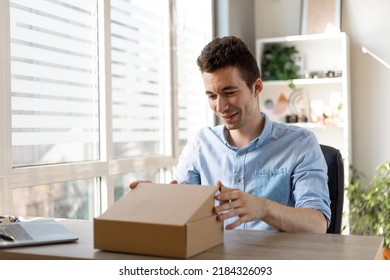 Happy Amazed Young Man Consumer Holding Opening Cardboard Box Sit On Sofa At Home, Order Postal Shipping Courier Delivery Concept
