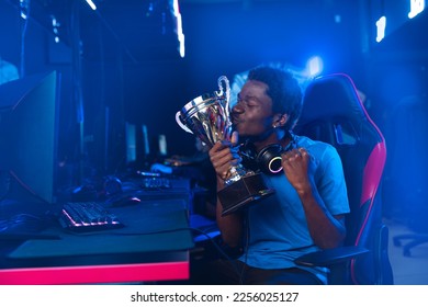 Happy American African Professional gamer, winner rejoices in victory of online games tournaments pc computer with headphones, Blurred red and blue background. - Shutterstock ID 2256025127
