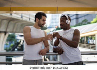 Happy American Bearded And African Black Men Toast And Drink Water After Running Workout In Modern City. Bodybuilding And Healthy Lifetstyle. Lovely LGBT Gay Couple Jogging Exercise.