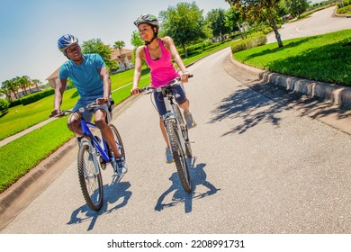 Happy American Couple Enjoying Leisurely Bike Ride Together On Suburban Street While Keeping Fit And Healthy