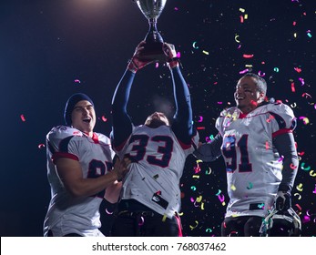 Happy American Football Team Celebrating Victory With Trophy And Confetti On The Night Field