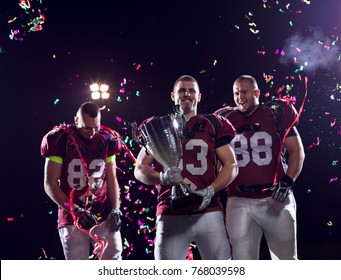 Happy American Football Team Celebrating Victory With Trophy And Confetti On The Night Field