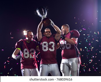 Happy American Football Team Celebrating Victory With Trophy And Confetti On The Night Field