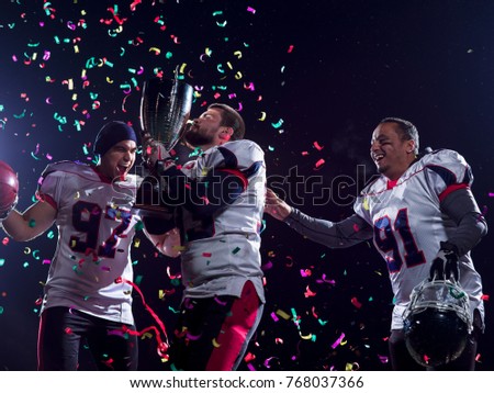 happy american football team celebrating victory with trophy and confetti on the night field