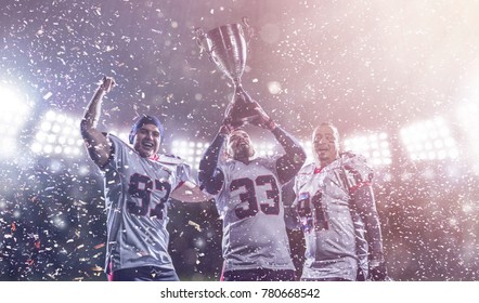 Happy American Football Team With Trophy Celebrating Victory In The Cup Final On Big Modern Stadium With Lights And Flares At Night